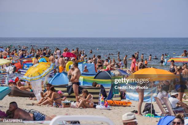 People enjoy hot summer weather , sunbathing and taking a dip in a cold sea waters , covering themselves from the wind by the windbreaks on the...