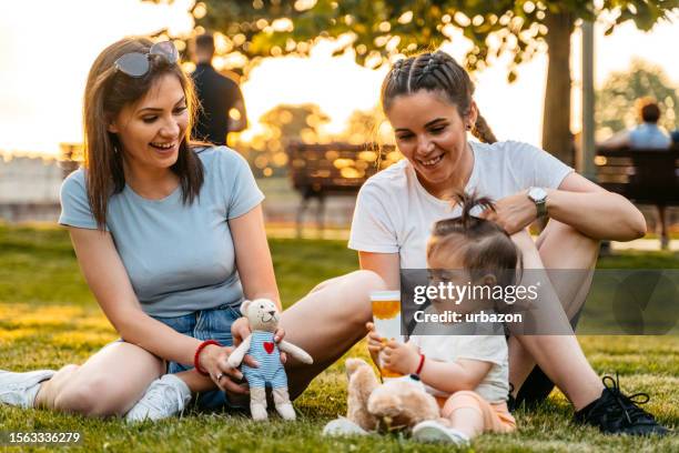 young mother and a friend playing with her baby girl in the park - godmother stock pictures, royalty-free photos & images