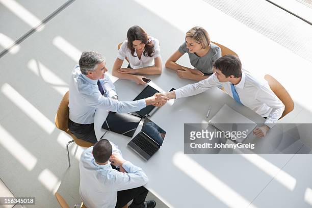 overhead view of a business group in a meeting shaking hands - business relationship stock pictures, royalty-free photos & images