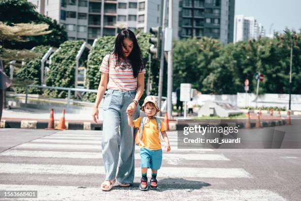 mother and son  carrying rucksack walking on zebra crossing on way to school - cross road children stockfoto's en -beelden