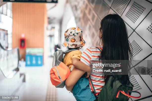 mutter und sohn tragen rucksack, während sie auf einer rolltreppe fahren und zur schule pendeln - toddler at airport stock-fotos und bilder