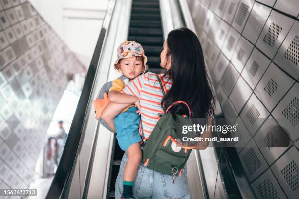 mutter und sohn tragen rucksack, während sie auf einer rolltreppe fahren und zur schule pendeln - baby bag stock-fotos und bilder