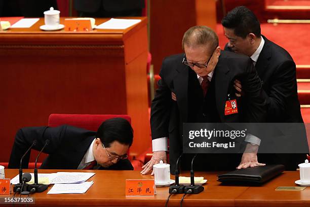 Former Chinese president Jiang Zemin gets helped standing up as President Hu Jintao goes down to pick up a document during the closing session of the...