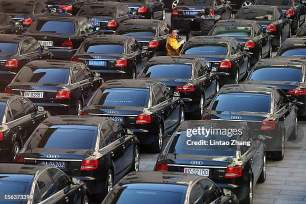 Driver waits amongst official cars, parked outside the Great Hall of the People, during the closing session of the 18th National Congress of the...