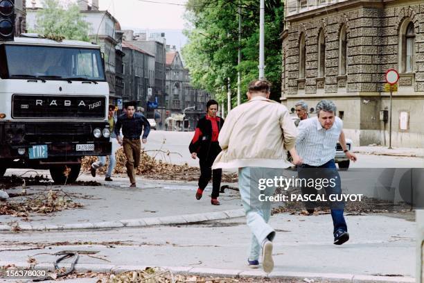 Bosnian civilians run for shelter across a street to avoid shelling from Serb irregulars in the Bosnian capital Sarajevo, on July 12, 1992.