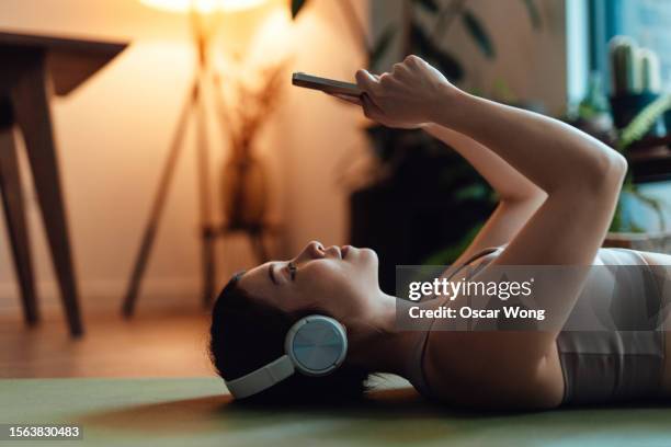 young asian woman using smartphone after workout at home - pilates stock pictures, royalty-free photos & images