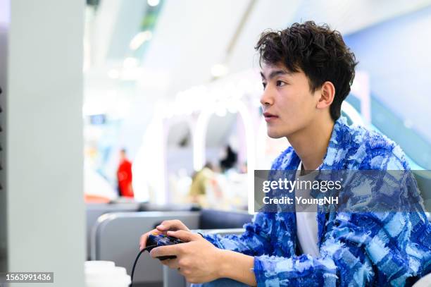 joven asiático jugando a un videojuego con un controlador de juego - video game fotografías e imágenes de stock