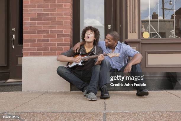 father watching son playing electric guitar - vater sohn musik stock-fotos und bilder