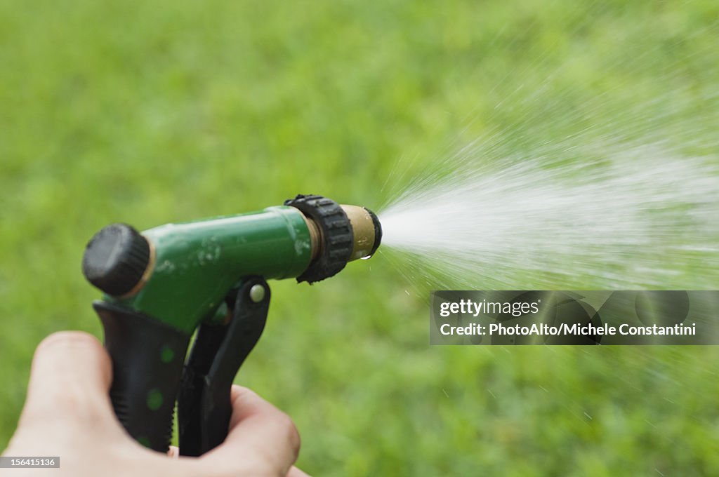 Person using spray nozzle on garden hose to water lawn, cropped