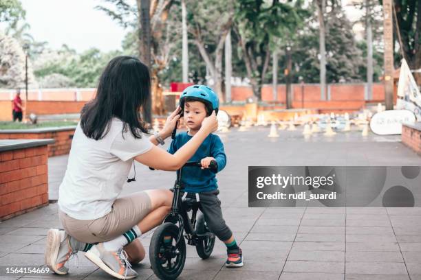 uma mãe ajudando seu filho pequeno a colocar seu capacete de bicicleta - tighten - fotografias e filmes do acervo