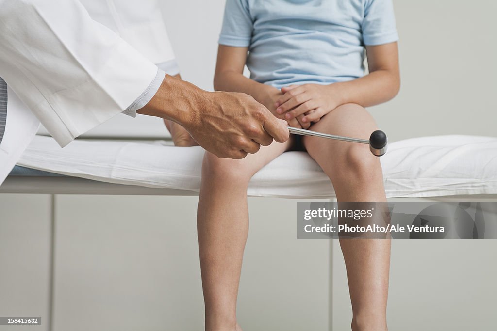 Doctor checking boy's reflexes with reflex hammer, cropped