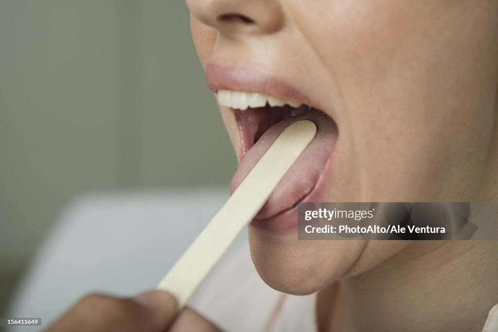 Woman having mouth examined with tongue depressor, cropped