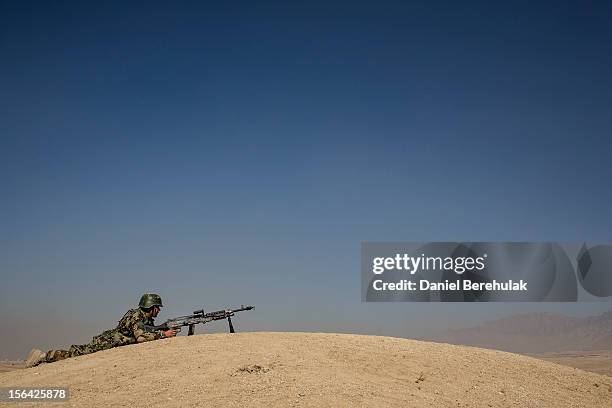 An Afghan National Army cadet takes cover on the edge of a hill as he prepaes to offer cover with his M-40 machine gun, armed with blanks, during a...