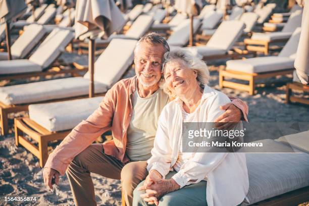 happy elderly couple sitting on sun loungers during summer vacation. - umbrella sun stock-fotos und bilder