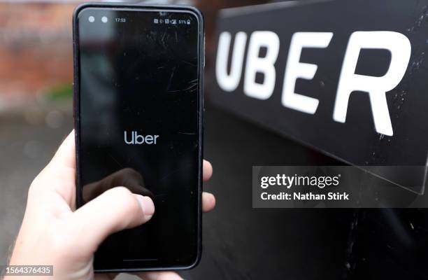 Phone is held next to a Uber car displaying the Uber app on July 22, 2023 in Holmes Chapel, England .