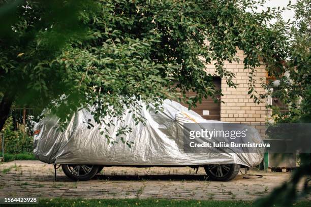 modern car standing on countryside yard covered by awning made of polyester that protecting automobile from ultraviolet light and overheating. - car sunshade stock pictures, royalty-free photos & images