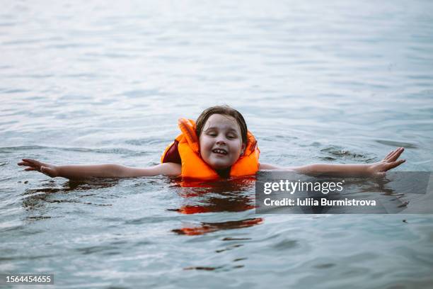 relaxed little girl wearing life vest enjoying safe swimming in river. - drowning girl stock pictures, royalty-free photos & images