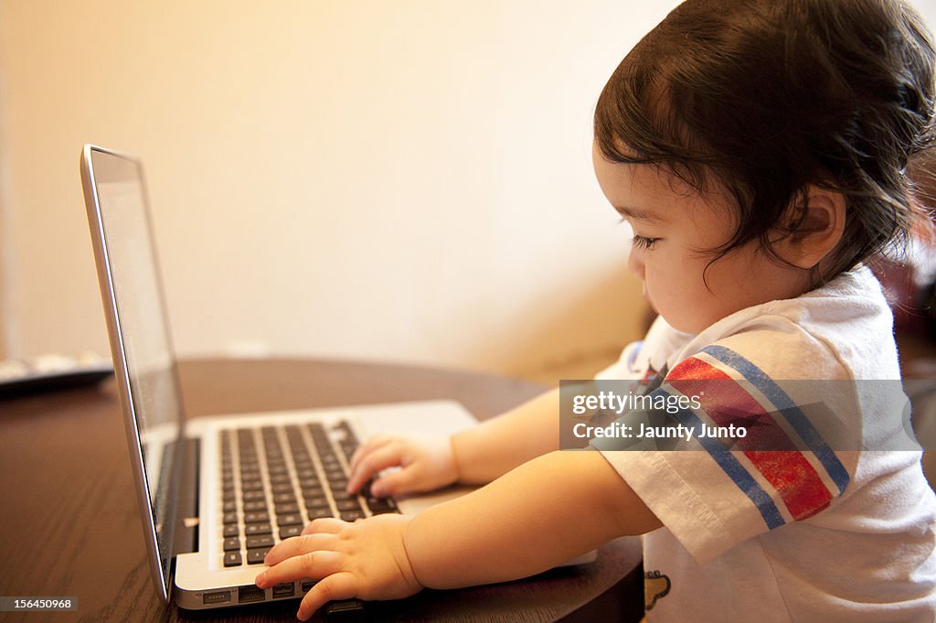 A baby boy playing with a laptop