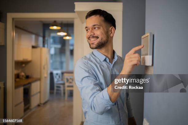 young man adjusts the temperature at home with a device on the wall - turning on or off stock pictures, royalty-free photos & images
