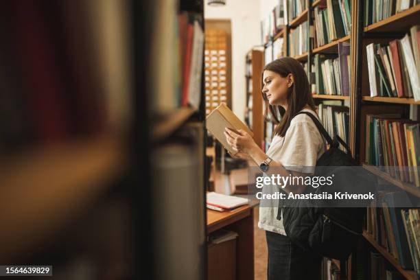 portrait of female student looking for special book in library. - book shop stock pictures, royalty-free photos & images