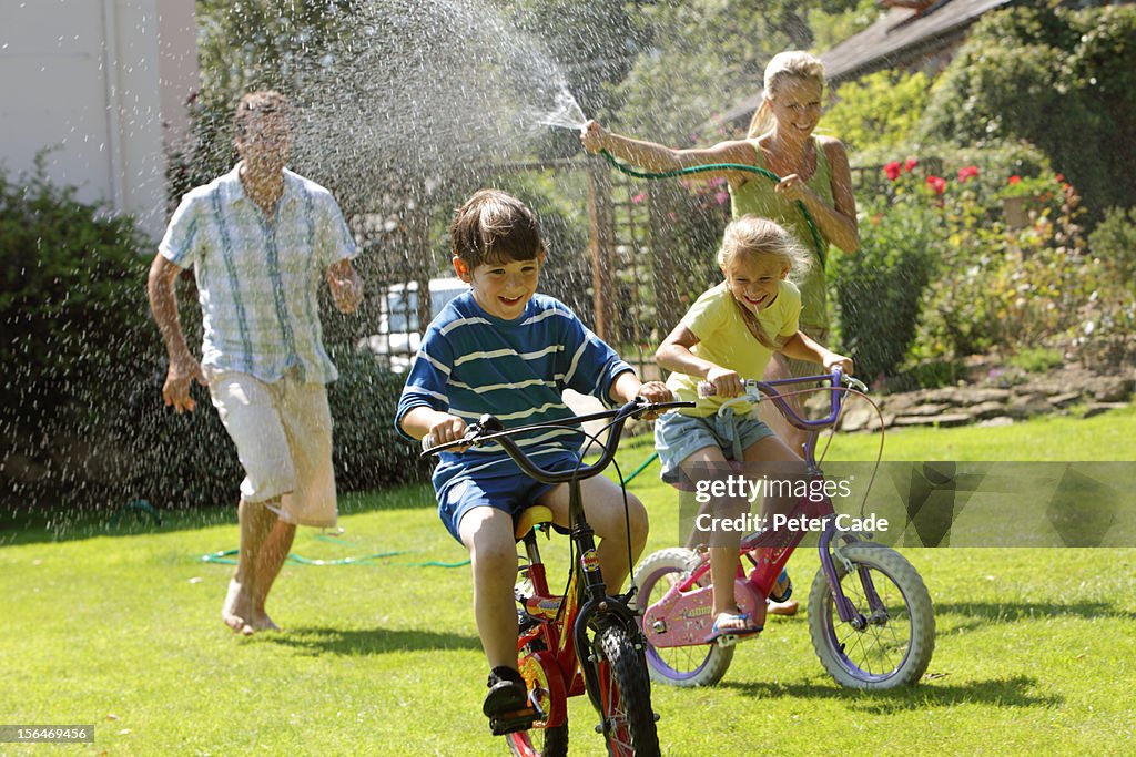 Family in garden with hosepipe, children on bikes