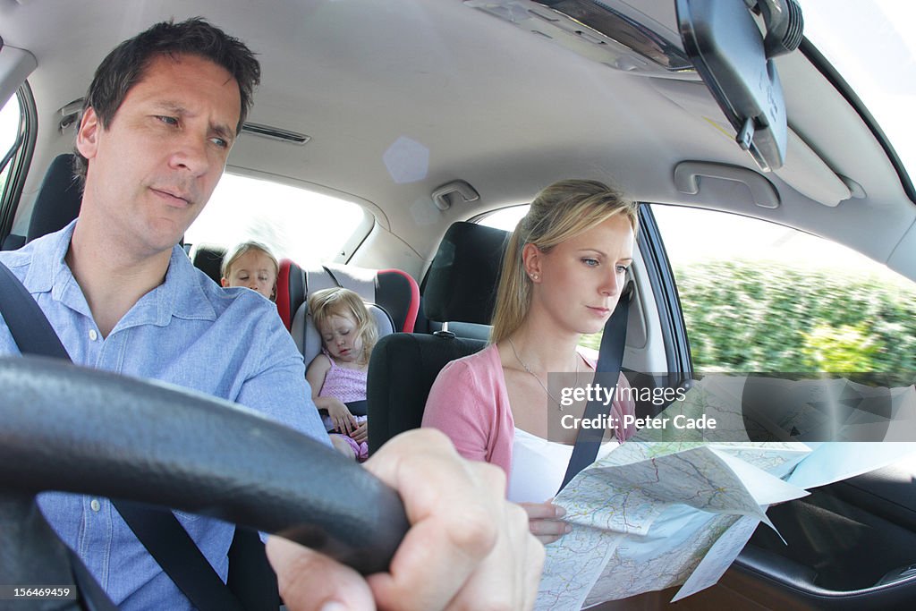 Family in car, children asleep, parents with map