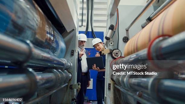 les ingénieurs industriels professionnels masculins parlent avec un ouvrier d’usine tout en utilisant un ordinateur portable dans une usine de fabrication. travailler dans une usine de fabrication ou une usine de production. - article de presse photos et images de collection