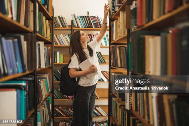 portrait of female student looking for special book in library. - book library stock pictures, royalty-free photos & images