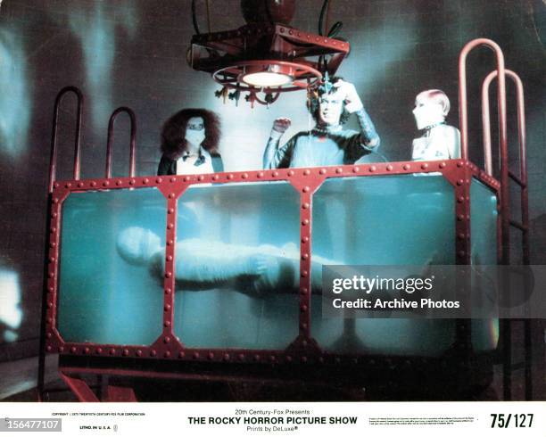 Patricia Quinn, Tim Curry and another woman stand over the submerged Rocky in a scene from the film 'The Rocky Horror Picture Show', 1975.