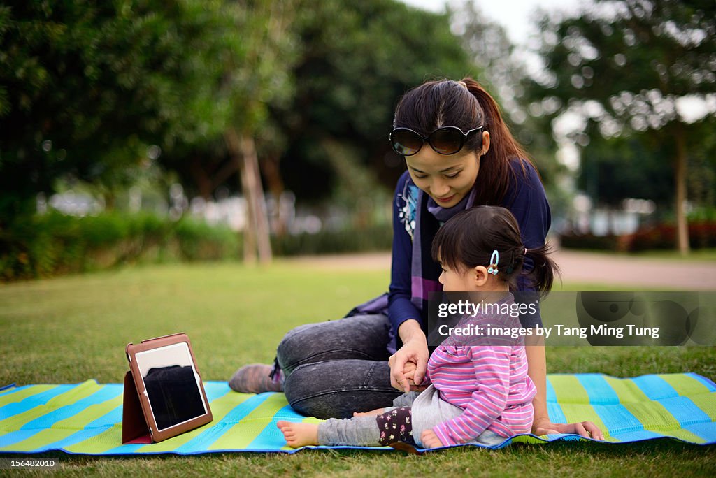 Mom and baby playing with a tablet pc on the grass