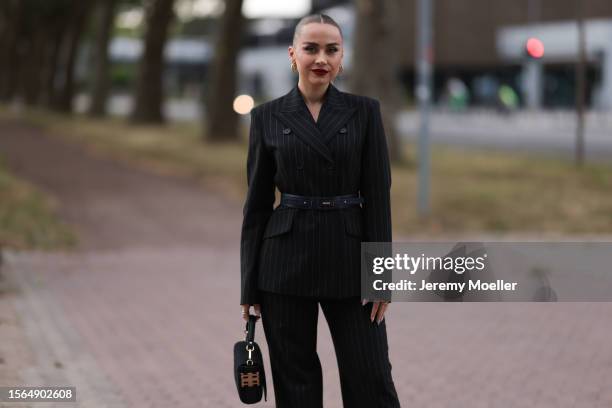 Anna Idriess is seen wearing a complete Riani outfit, consisting of a black pinstriped two-piece with suit pants and a blazer, a black leather belt,...