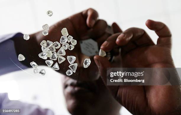 An employee is seen from below using a magnifier to inspect a selection of uncut diamonds in this arranged photograph at DTC Botswana, a unit of De...