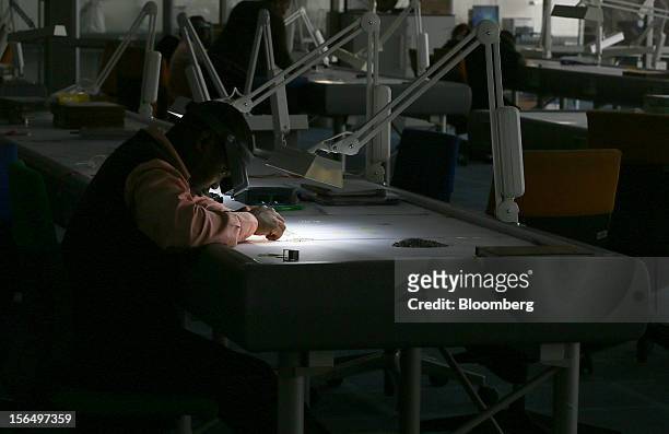 An employee uses an angled light and a magnifier to illuminate uncut diamonds at a sorting table in DTC Botswana, a unit of De Beers, in Gaborone,...
