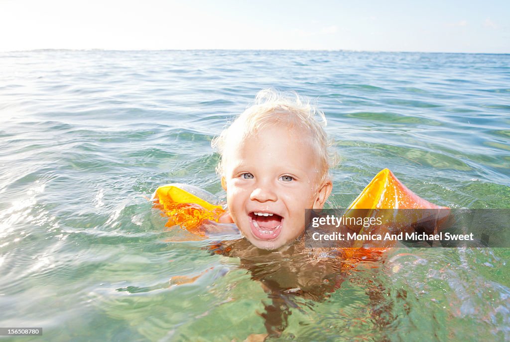 Excited young boy in the ocean with water wings