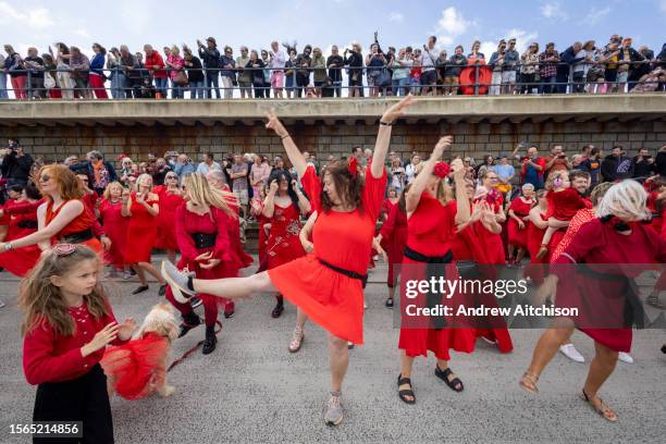 Hundreds of Kate Bush fans came together wearing red dresses on Folkestone's Harbour Arm to dance to her most iconic song, Wuthering Heights on the...