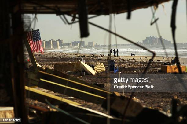 People walk along a beach amidst debris in the heavily damaged Rockaway neighborhood where a large section of the iconic boardwalk was washed away on...