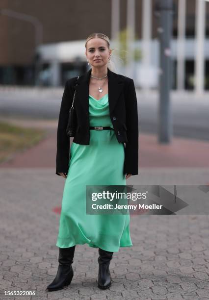Kim Engel is seen wearing a black blazer, underneath a green midi dress with a black belt, a black bag and black boots outside during the Riani...