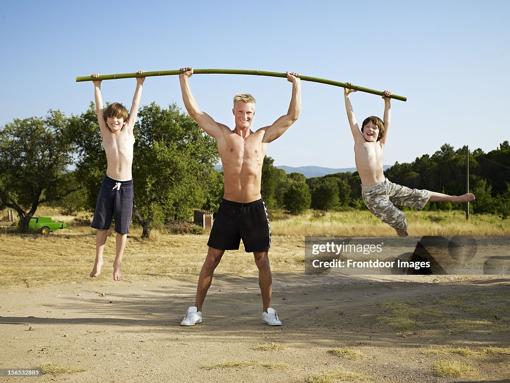 Young man lifting two young boys with a bamboo bar