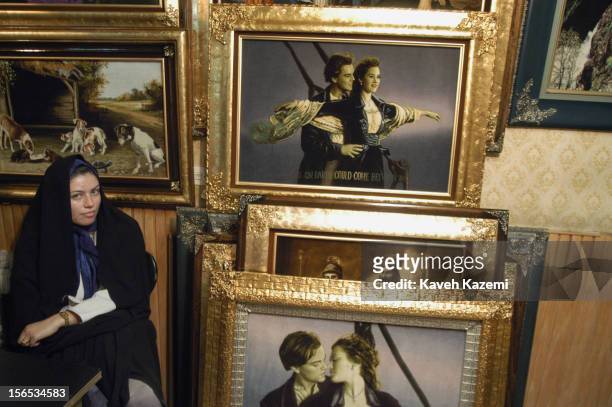 Woman in black chador sits next to paintings depicting Leonardo DiCaprio and Kate Winslet from the movie 'Titanic'.