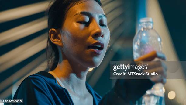 closeup of happy young sporty asian woman wear sports outfits drinking water from bottle through the city streets over bridge at night. running club and exercise outdoor. - hot latin nights stock pictures, royalty-free photos & images