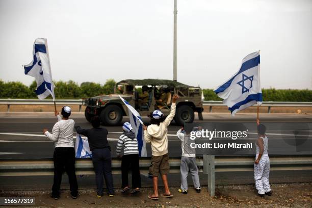 Israeli children wave their national flag as they greet an army convoy passing on a road leading to the Israel-Gaza border near the southern Israeli...