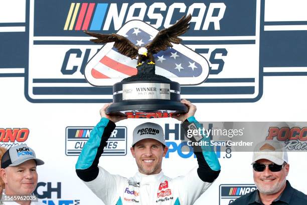 Denny Hamlin, driver of the Mavis Tires & Brakes Toyota, lifts the HighPoint.com 400 trophy in victory lane after winning the NASCAR Cup Series...