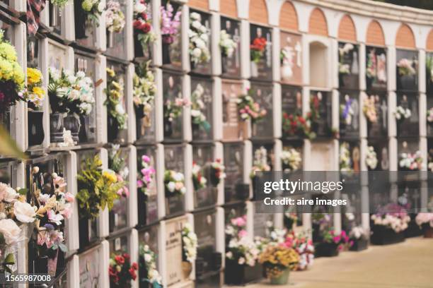 cemetery wall tombs with decorative flowers attached, side view on a sunny day without people - cementerio fotografías e imágenes de stock