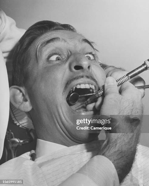 Middle-aged man appears anxious as he sits in the dentist chair undergoing a routine dental procedure.