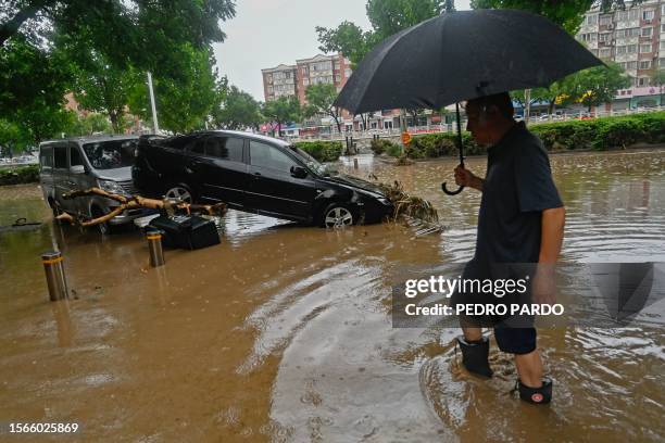 Man wades past a damaged car along a flooded street, after heavy rains in Mentougou district in Beijing on July 31, 2023. Heavy rains battered...