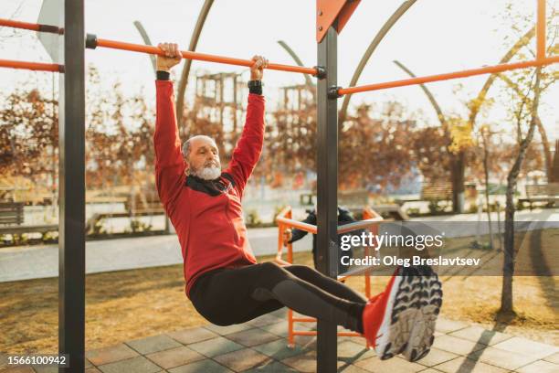 senior man lifting legs up to the body on horizontal bar to train abs muscles - lift stock pictures, royalty-free photos & images