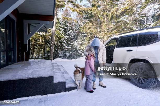 the girl says goodbye to her grandmother, who is about to leave in a car parked near a country house. next to the dog. - auto von hinten winter stock-fotos und bilder