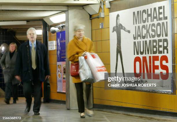 Commuters in London's underground walk past a poster advertising pop singer Michael Jackson's lastest CD, "Michael Jackson Number Ones" 19 December,...