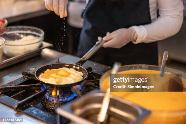 a chef prepares an omelet or scrambled eggs in a restaurant kitchen. she seasons the food with salt and pepper - cooking gas stock pictures, royalty-free photos & images
