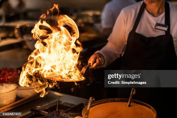 pro chef flambeing in the kitchen in a pan on a gas-fired stove. - wok stockfoto's en -beelden